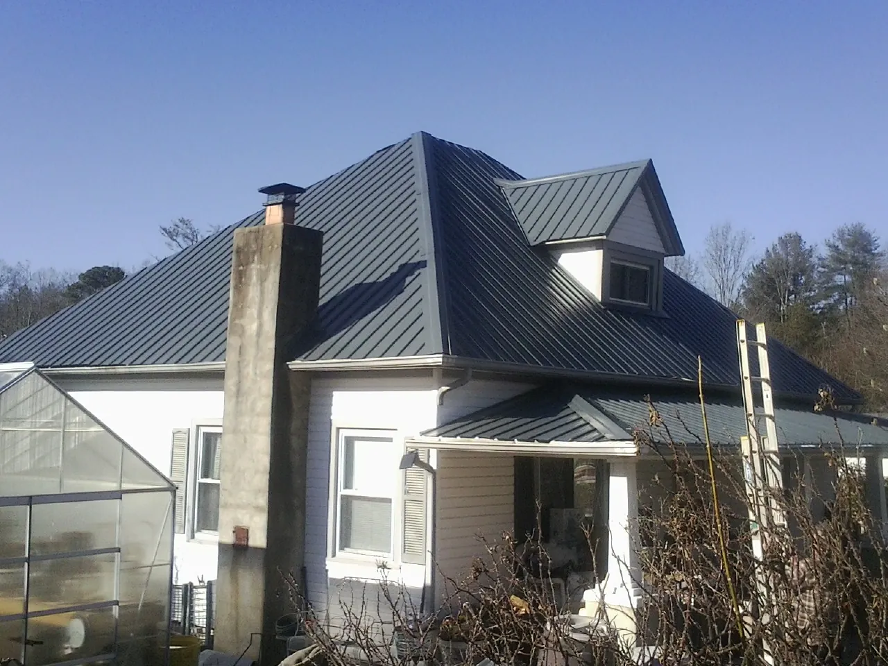 Dark blue standing seam metal roof on a white farmhouse with dormer — Slate & Tile Roof Repair by Roofing Brothers in West Salem